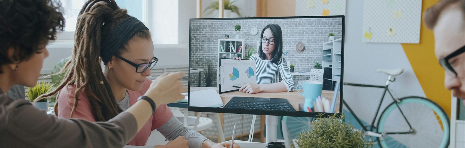 Équipe réunie autour d'un écran pour une visioconférence avec un collègue, dans un bureau coloré